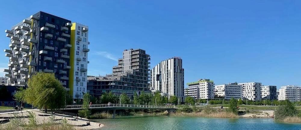 Modern apartment buildings and a pedestrian bridge beside a lake