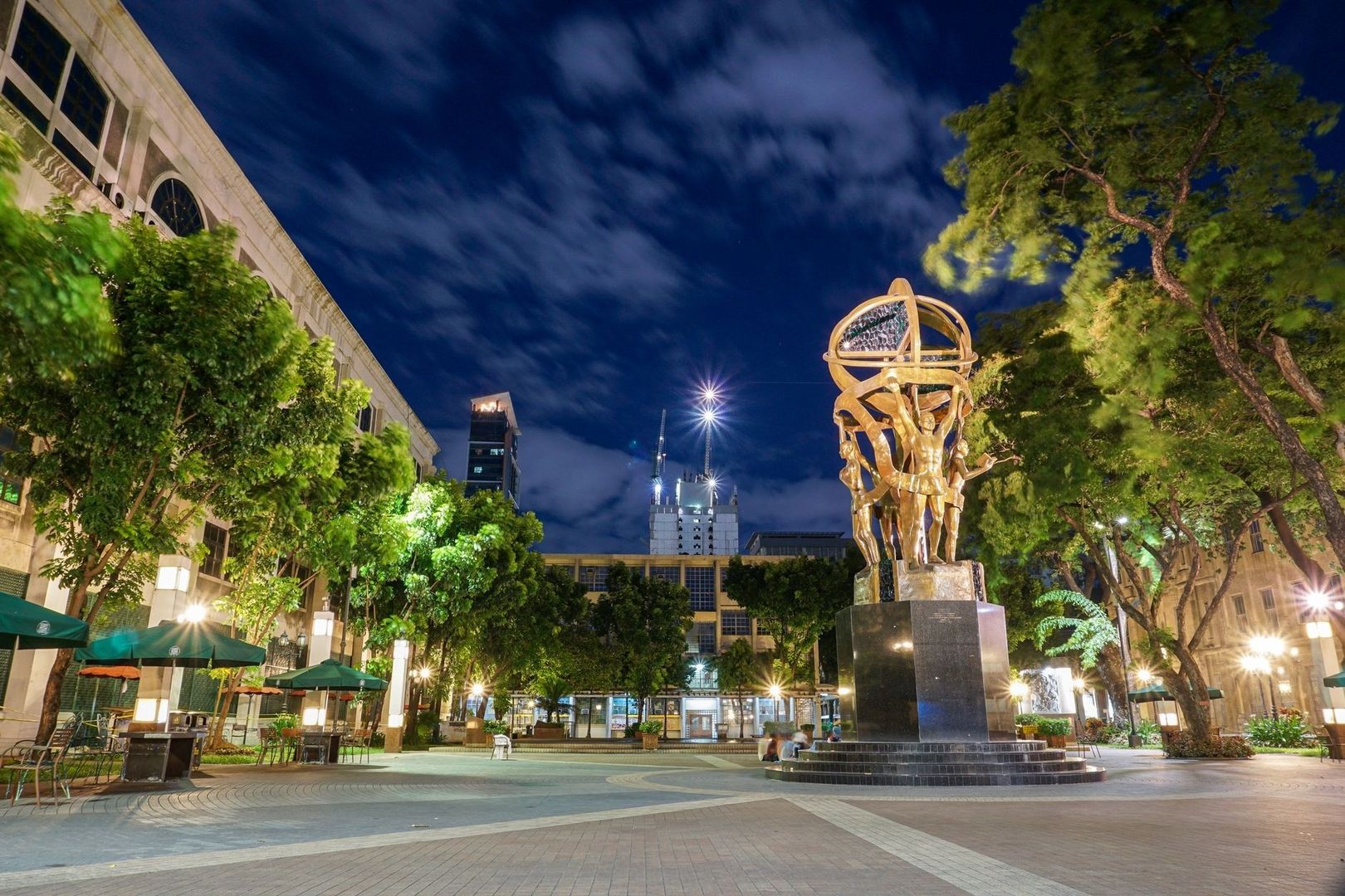 Illuminated public sculpture anchors a landscaped urban square at night